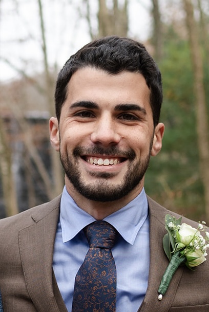 Zachary Denning, photographed outdoors in a brown suit with a white flower on the lapel